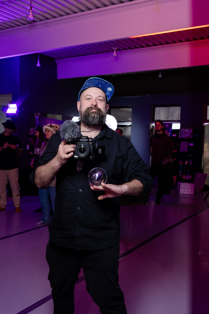 Kiamythos Films camera operator holding a camera and glass sphere in purple event light.