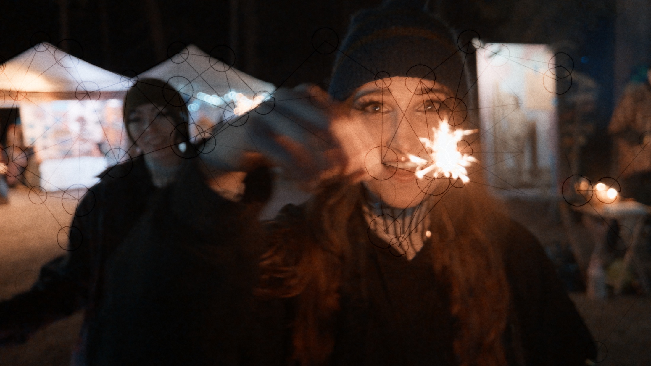 A performer looking into the camera while holding a sparkler at night.